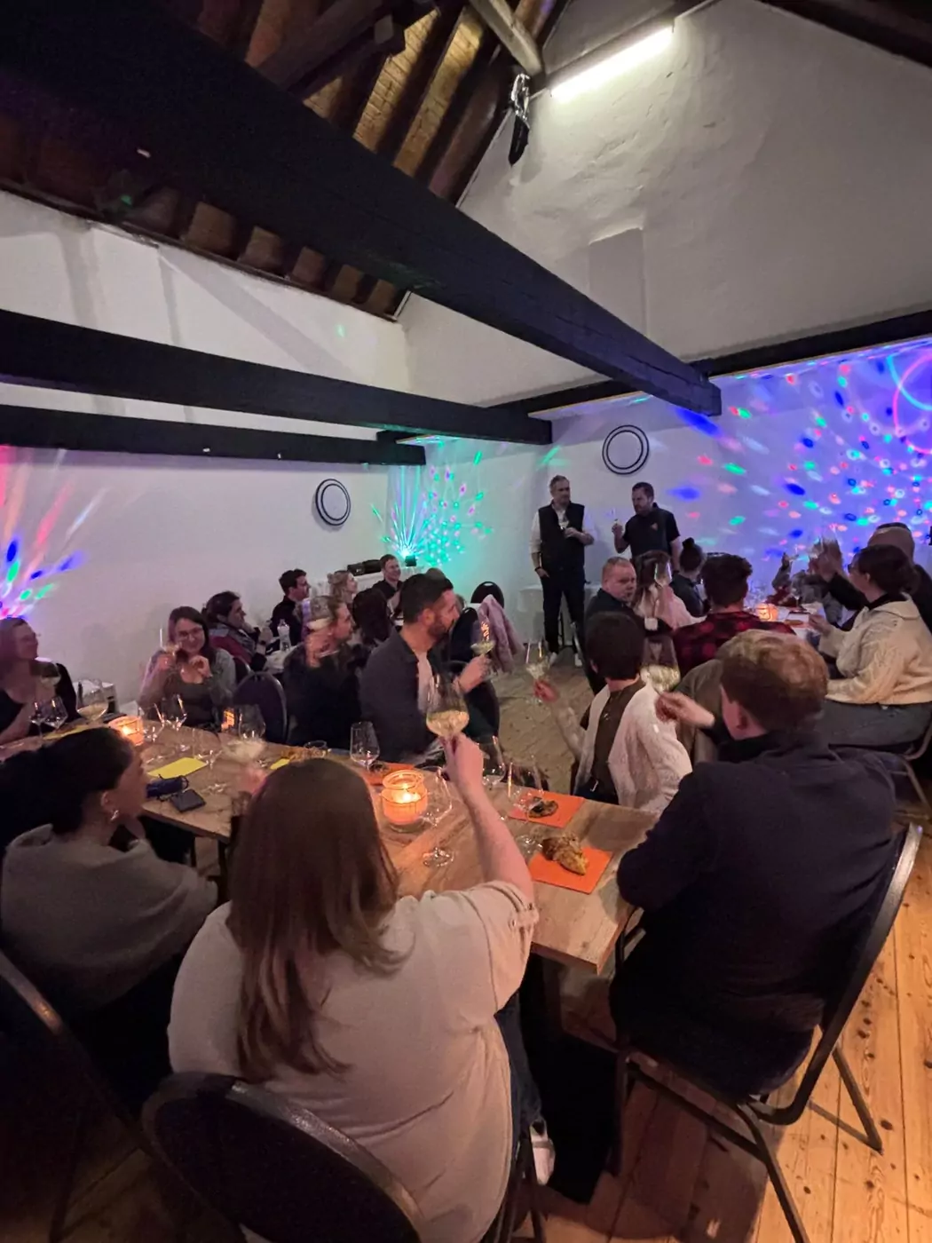 Eventscheune am Abend mit Disco-Licht und feiernder Gruppe an gedeckter Tafel