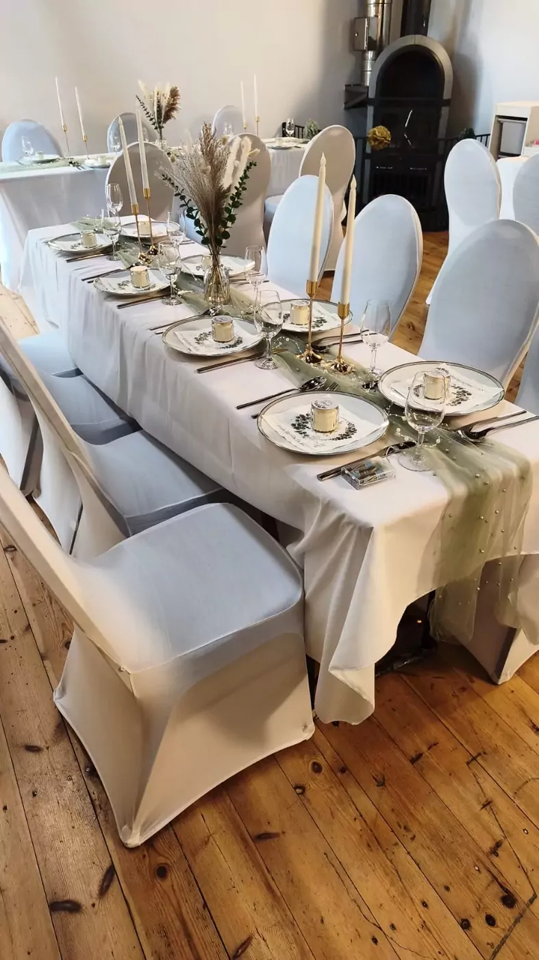 Festlich gedeckte Tafel mit weißen Hussen, grünem Tischläufer und Trockenblumen