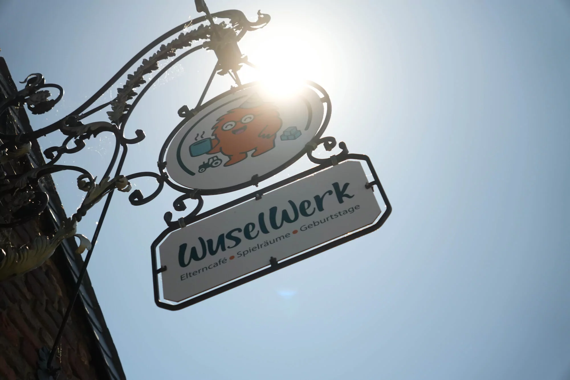 WuselWerk-Hängeschild gegen blauen Himmel — Eltern-Café · Spielräume · Geburtstage