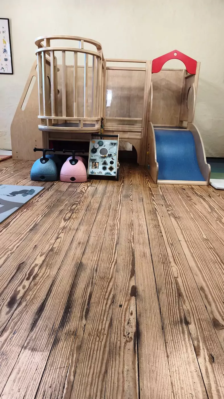 Holz-Spielturm mit blauer Rutsche und Bobby-Cars im Indoor-Spielraum